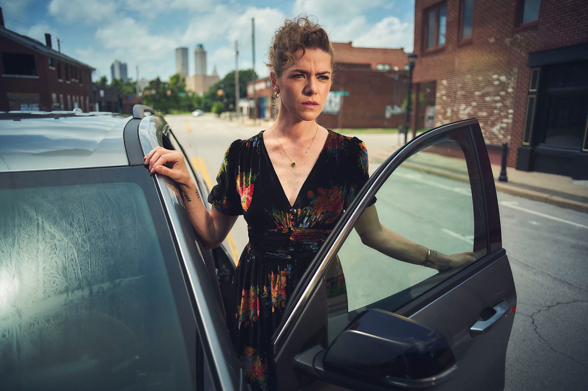 Kaniehtiio Horn, in a dark floral dress, stands in the open door of a car on a city street.