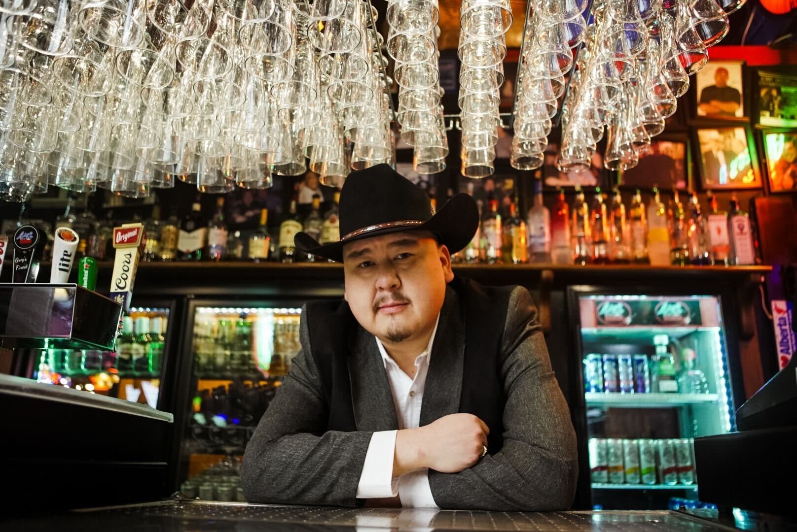 William Prince in a black cowboy hat, leaning on a bar.
